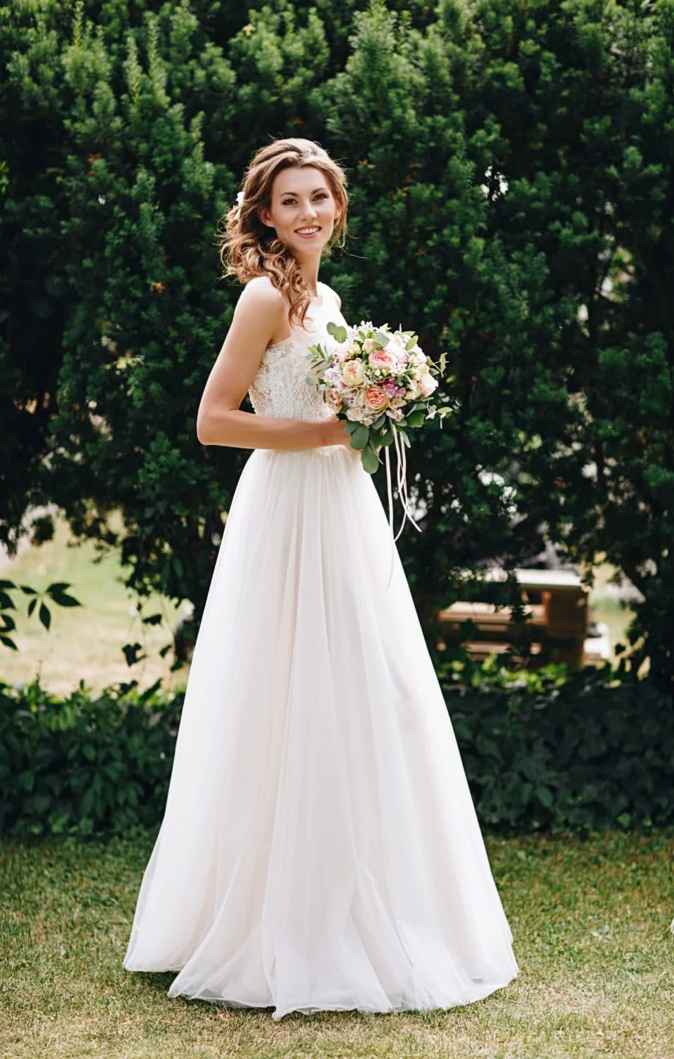 Bride in a white wedding dress with a full skirt, holding her bouquet in a garden