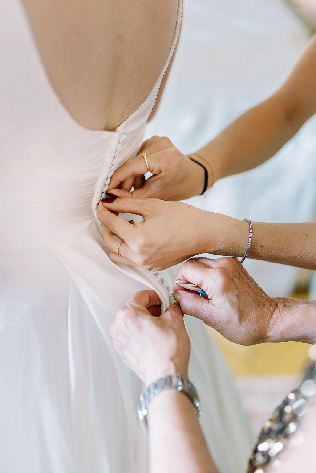 Close-up of the buttons being fastened at the back of a wedding dress