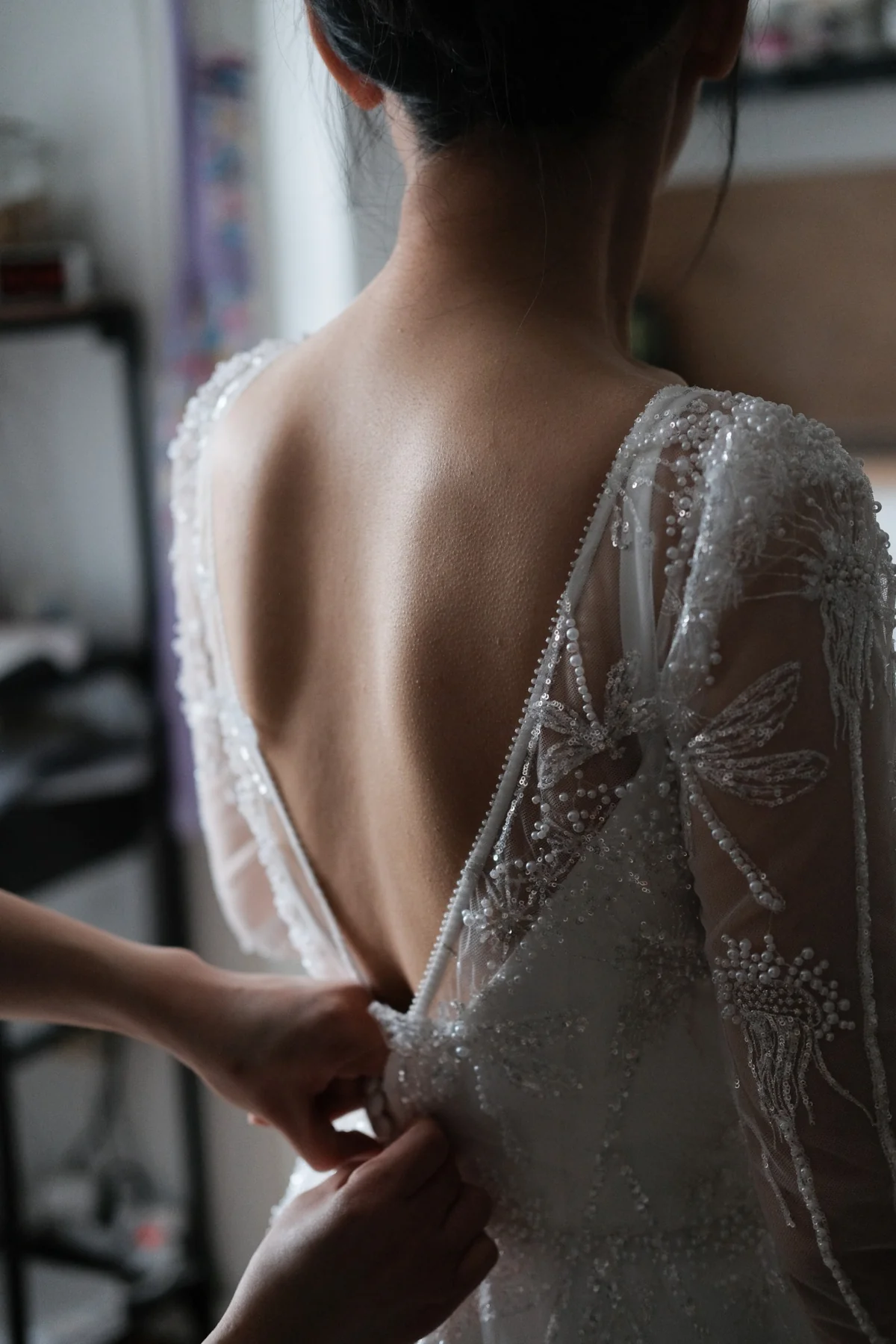 Back view of a wedding dress with a low neckline and delicate beaded details as the bride gets ready