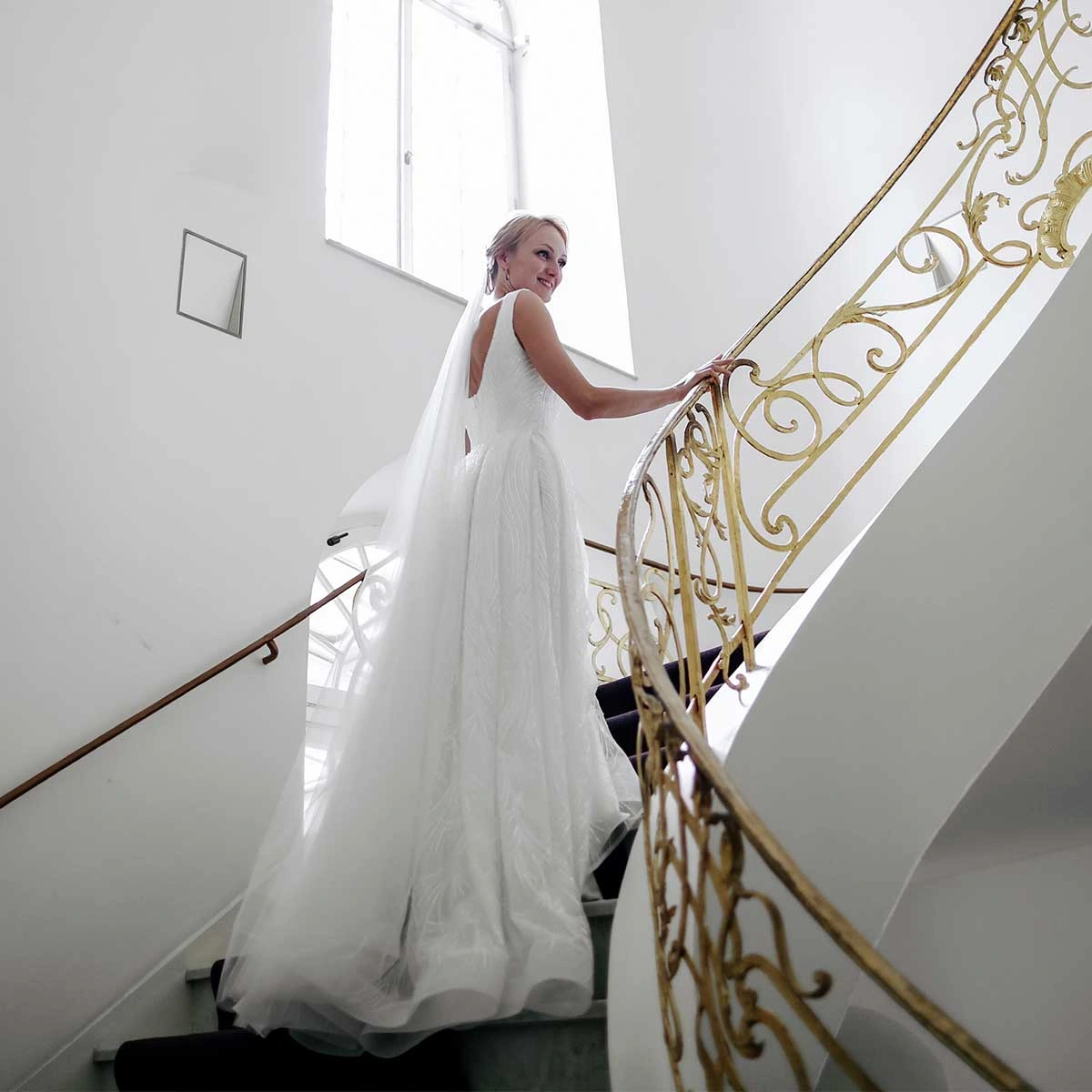 Braut im FRILISA Kleid auf einer Treppe mit goldenem Geländer