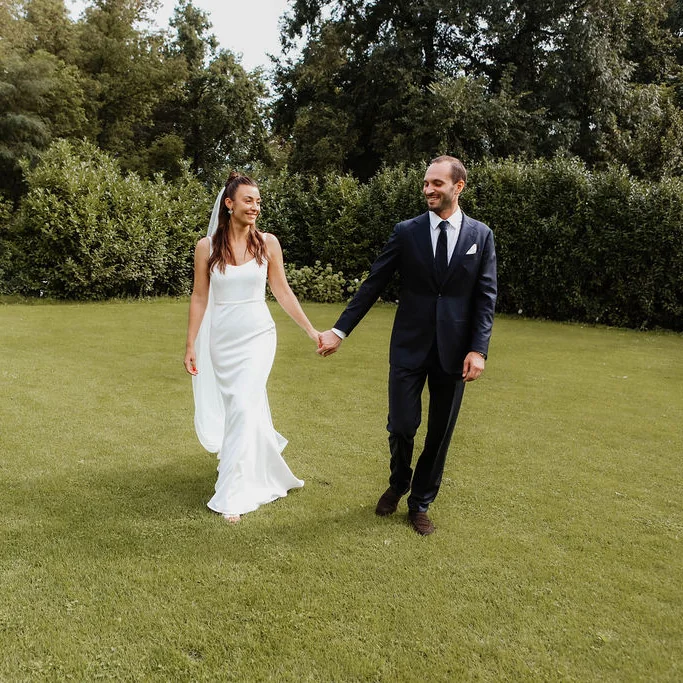 Bride and groom holding hands in a garden, the bride wearing a slim-fitting wedding dress