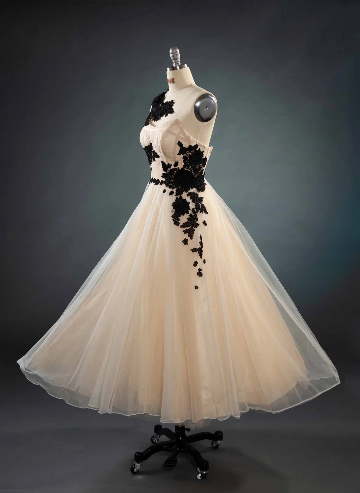 Elfenbeinfarbenes Abendkleid mit weitem Tüllrock und schwarzen Blütenapplikationen auf einer Schneiderpuppe