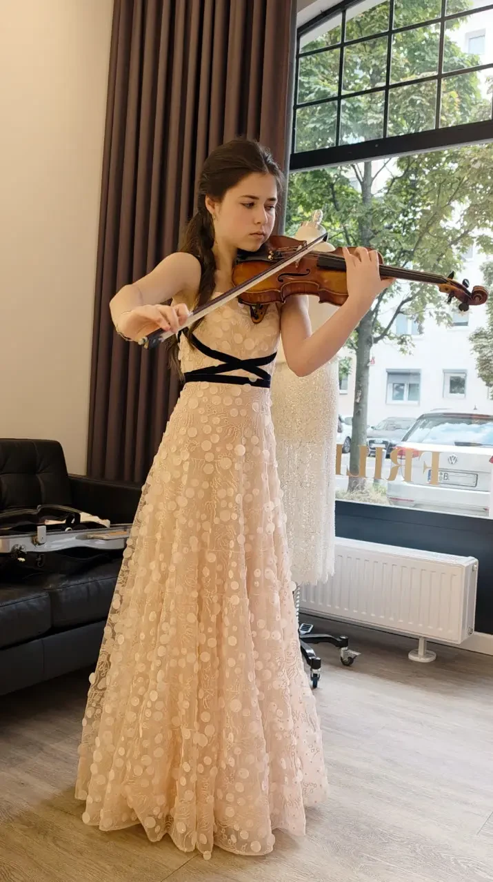 Shira Fuchs spielt Violine in ihrem puderfarbenen FRILISA Konzertkleid mit marineblauen Samtbändern